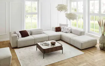 Zwei lachende Frauen in moderner Einrichtung neben einem grauen Cord-Sofa mit Longchair. Kombination aus Wohlfühlatmosphäre, modernen Möbeln und urbanem Lifestyle.